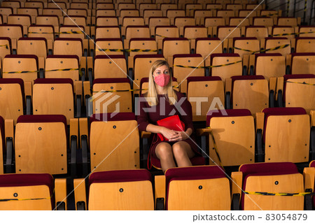 Reflective woman in protective mask sitting alone in empty cinema house 83054879