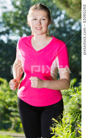Athletic woman in pink T-shirt is running around 83060268