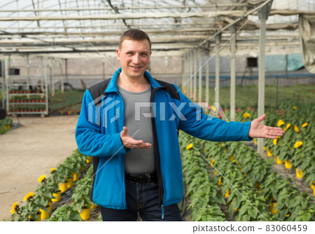 Portrait of man gardener who is standing on his work place in greenhouse. 83060459