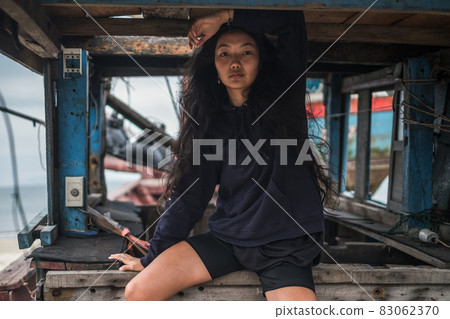 sitting in old wooden ship and looking at camera with copy space. Long black curly hair. Street style portrait. High quality photo sitting in old wooden ship and looking at camera with copy space. Long black curly hair. Street style portrait. High quality photo 83062370