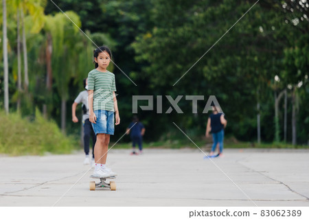 Asian child girl learning to skateboard outdoors. Kid having fun and playing skateboard on the road at the day time. Kid activity and extreme sport concept. Asian child girl learning to skateboard outdoors. Kid having fun and playing skateboard on the road at the day time. Kid activity and extreme sport concept. 83062389