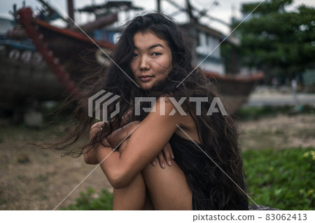 sitting, holding her legs and relaxing. Brunette with long hair posing. Looking at camera with copy space. Wind in her hair. . High quality photo 83062413