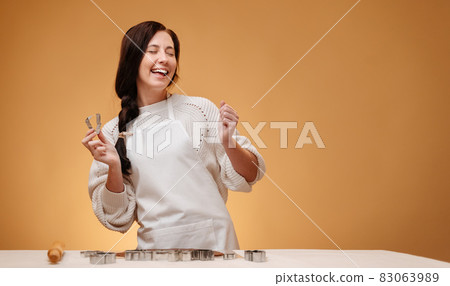 Woman confectioner laughing prepares cookies cutting out metal forms. 83063989