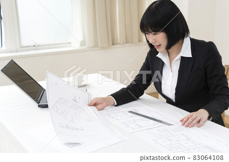 Woman looking at architectural drawings at desk 83064108