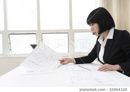 Woman looking at architectural drawings at desk 83064109