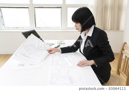 Woman looking at architectural drawings at desk 83064111