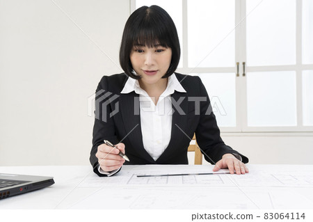 Woman looking at architectural drawings at desk 83064114