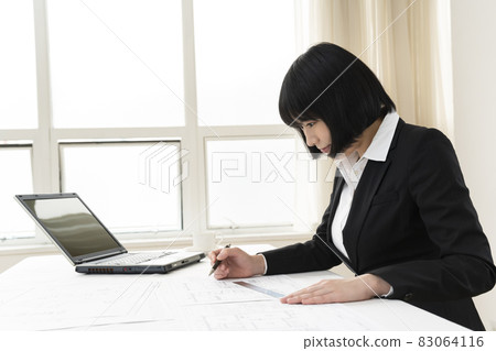 Woman looking at architectural drawings at desk 83064116