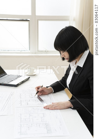 Woman looking at architectural drawings at desk 83064117