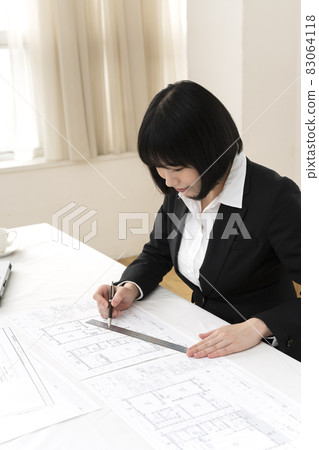 Woman looking at architectural drawings at desk 83064118