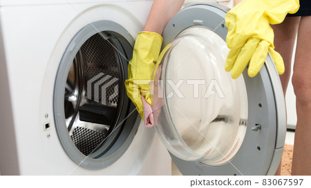 Women's hands in yellow rubber gloves wash the glass of the washing machine door Women's hands in yellow rubber gloves wash the glass of the washing machine door 83067597