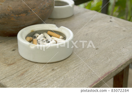 Cigarette stubs and ash in a ashtray on wooden table 83072284