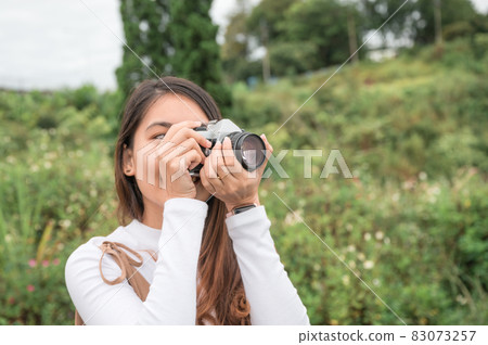 Young asian woman taking photo with retro film camera among the nature in the morning Young asian woman taking photo with retro film camera among the nature in the morning 83073257