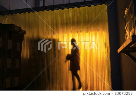 Yellow plastic curtain entrance with shadow of worker and cardboard package in warehouse 83073292