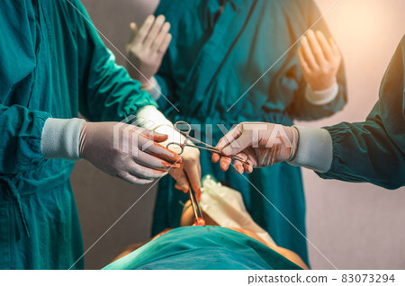 Surgeons team performing surgery and passing surgical scissors on injured patient in operating room Surgeons team performing surgery and passing surgical scissors on injured patient in operating room 83073294