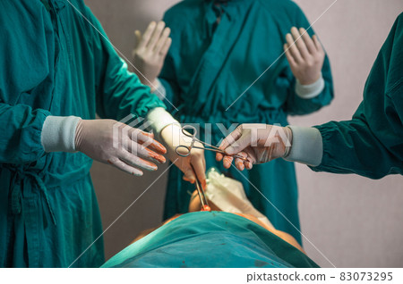 Surgeons team performing surgery and passing surgical scissors on injured patient in operating room 83073295