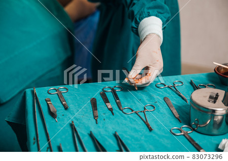 Surgeon wearing medical glove choosing surgical instrument on table in the operating room 83073296