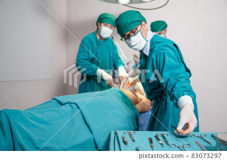 Team surgeon choosing scalpel while operating seriously injured patient in operating room Team surgeon choosing scalpel while operating seriously injured patient in operating room 83073297