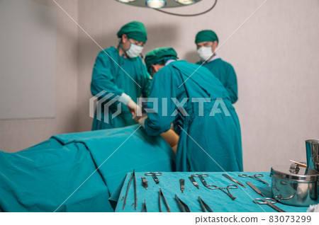 Surgeons team performing surgery a seriously injured patient and picking up medical equipment in operating room at hospital 83073299