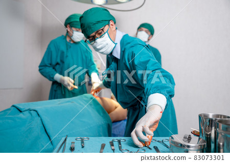 Team surgeon choosing scalpel while operating seriously injured patient in operating room Team surgeon choosing scalpel while operating seriously injured patient in operating room 83073301