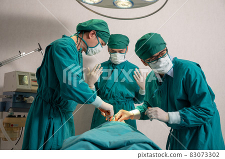 Surgeons team in surgical gown performing surgery a seriously injured patient in operating room at hospital Surgeons team in surgical gown performing surgery a seriously injured patient in operating room at hospital 83073302
