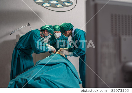 Surgeons team performing surgery a seriously injured patient through medical monitor in operating room at hospital 83073303