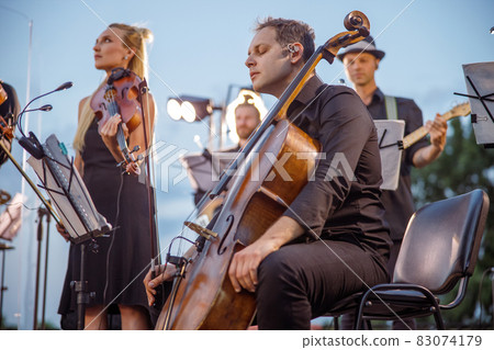 Male cellist playing in orchestra at outdoor concert 83074179