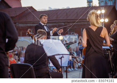 Conductor directing orchestra performance on the street 83074181
