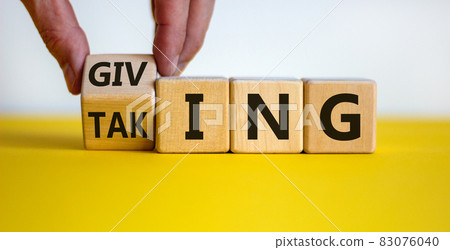 Taking or giving symbol. Hand turns a cube and changes the word 'taking' to 'giving' on wooden cubes. Beautiful yellow table, white background, copy space. Business and taking or giving concept. Taking or giving symbol. Hand turns a cube and changes the word 'taking' to 'giving' on wooden cubes. Beautiful yellow table, white background, copy space. Business and taking or giving concept. 83076040