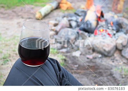 Balancing a glass of wine on a knee against a campfire 83076183