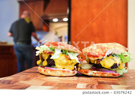 Two keto burgers sit on a table with a blurred kitchen and man in the background 83076242