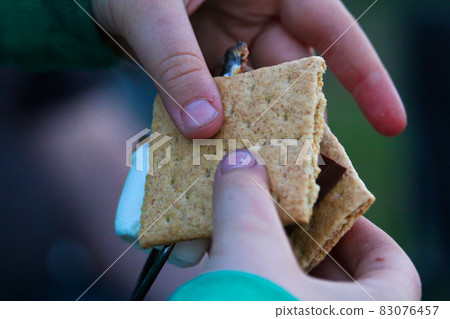 Hands pulling a marshmallow off a skewer to make a smore Hands pulling a marshmallow off a skewer to make a smore 83076457