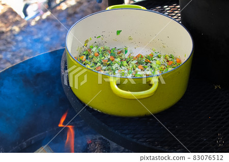 A green pot of chopped vegetables being cooked on a campfire 83076512