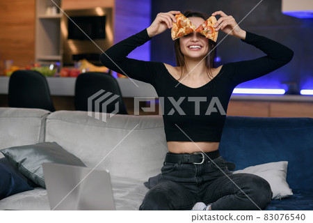 Happy beautiful girl with perfect smile having fun with pizza at home. Woman has dinner, enjoying meal. Leisure concept. Happy beautiful girl with perfect smile having fun with pizza at home. Woman has dinner, enjoying meal. Leisure concept. 83076540