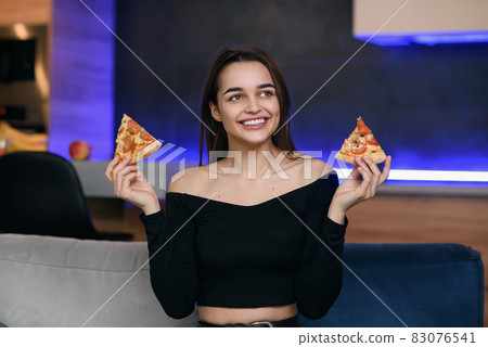 Happy beautiful girl with perfect smile having fun with pizza at home. Woman has dinner, enjoying meal. Leisure concept. Happy beautiful girl with perfect smile having fun with pizza at home. Woman has dinner, enjoying meal. Leisure concept. 83076541