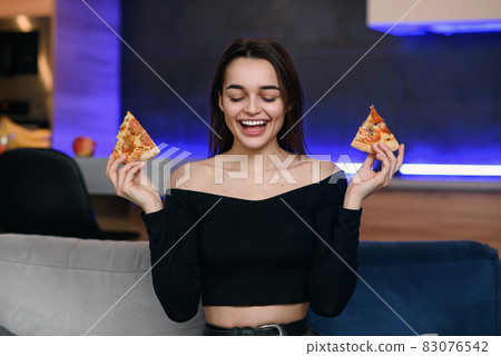 Happy beautiful girl with perfect smile having fun with pizza at home. Woman has dinner, enjoying meal. Leisure concept. 83076542