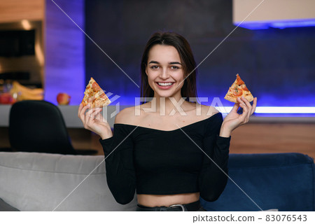 Happy beautiful girl with perfect smile having fun with pizza at home. Woman has dinner, enjoying meal. Leisure concept. Happy beautiful girl with perfect smile having fun with pizza at home. Woman has dinner, enjoying meal. Leisure concept. 83076543