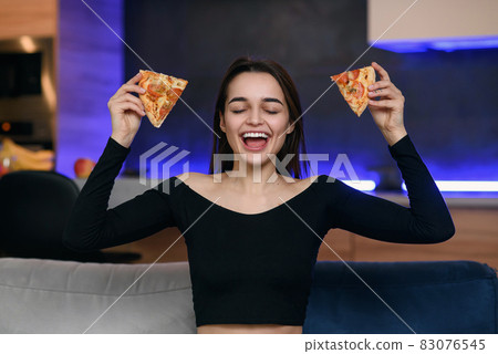 Happy beautiful girl with perfect smile having fun with pizza at home. Woman has dinner, enjoying meal. Leisure concept. 83076545