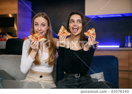 Two women having fun at home, opening pizza box, food delivery, home party 83076549