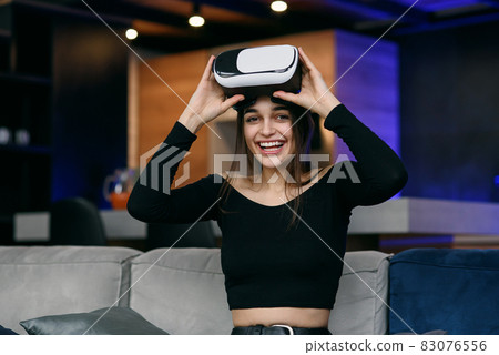 Likable joyful satisifed 25-aged woman putting on augmented reality goggles and working on virtual screen in the contemporary apartment Likable joyful satisifed 25-aged woman putting on augmented reality goggles and working on virtual screen in the contemporary apartment 83076556