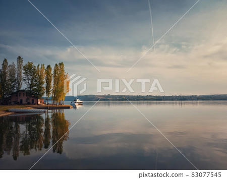 Scenic view with a house on the riverbank of Nistru river and a yacht floating. Autumn season landscape, colorful trees and beautiful sky reflected on the water surface 83077545