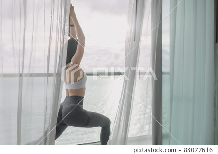 Woman does yoga warrior pose on the balcony with sea view. 83077616