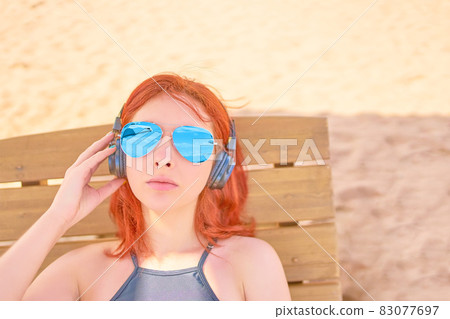 Beautiful woman in sunglasses listening to music on the beach. Beautiful woman in sunglasses listening to music on the beach. 83077697