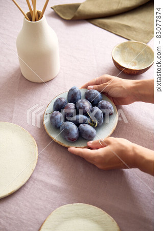 Fresh juicy sweet plums on an unusual clay plate. The girl serves the table. 83077874