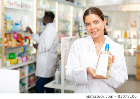 Portrait of a smiling young female pharmacist, demonstrating recently received goods for sale Portrait of a smiling young female pharmacist, demonstrating recently received goods for sale 83078106