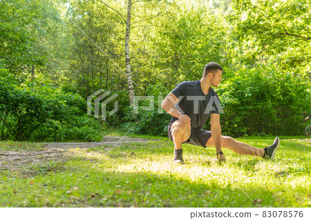 A young enduring athletic athlete is doing stretching in the forest outdoors, around the forest, oak trees.active exercise, trail athletic recreation jog, woods wellbeing. Autumn leisure feet 83078576