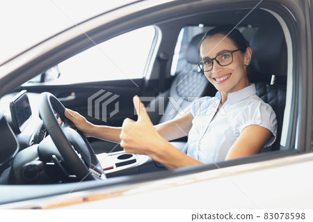 Portrait of smiling woman driving new car shows thumbs up closeup Portrait of smiling woman driving new car shows thumbs up closeup 83078598