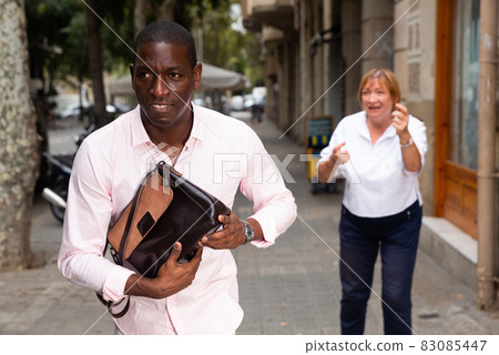 Street thief running away after stealing handbag from woman Street thief running away after stealing handbag from woman 83085447