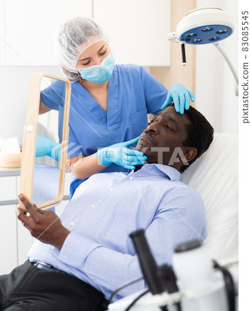 Man looking at mirror while cosmetician explaining facial procedure 83085545