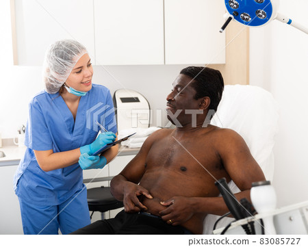 Female cosmetologist examining body of man before procedure 83085727